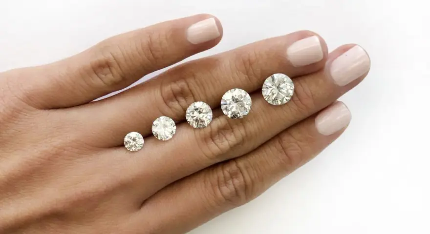Five round brilliant cut diamonds are displayed on a hand, showing a progression in size. The largest diamond is what is considered a big diamond.