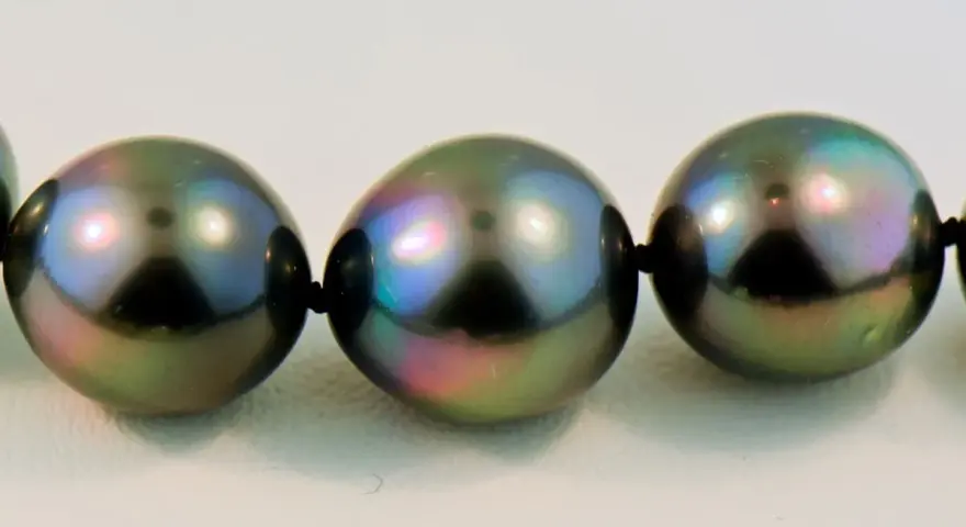 A close-up of a strand of dark, iridescent pearls with peacock green and purple overtones.