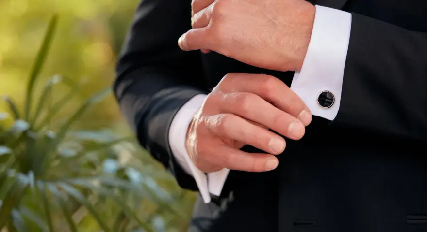 A man fastens his tuxedo cuff with elegant, black onyx cufflinks, showcasing classic types of cufflinks.