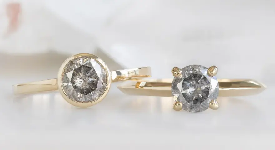 Two gold rings, one with a bezel setting and the other with a prong setting, showcase their unique diamond styles.