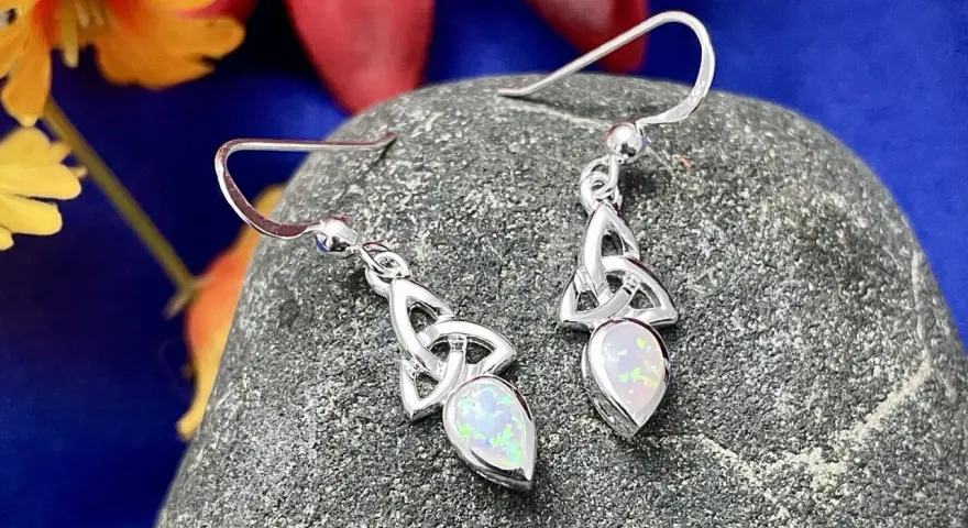 Silver Celtic knot earrings with opals, reminiscent of ancient Celtic birthstones, rest on a textured stone.
