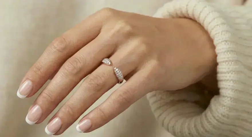 A hand with French manicured nails wears a sparkling rose gold ring. Rose gold is far from out of style!