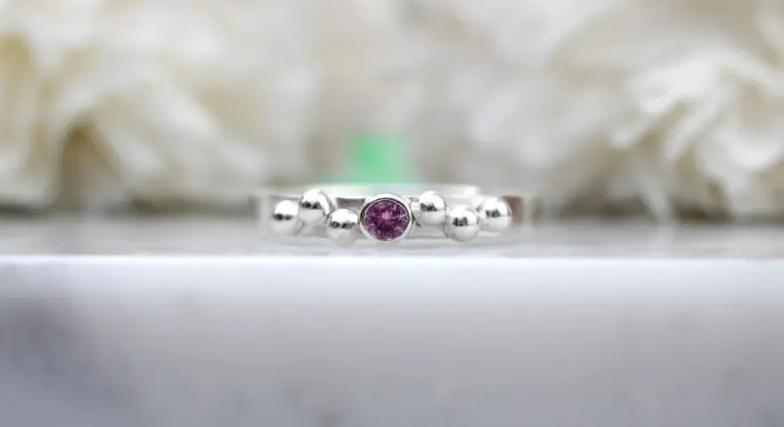 A silver ring with a central pink sapphire, the birthstone for September, surrounded by small silver spheres.