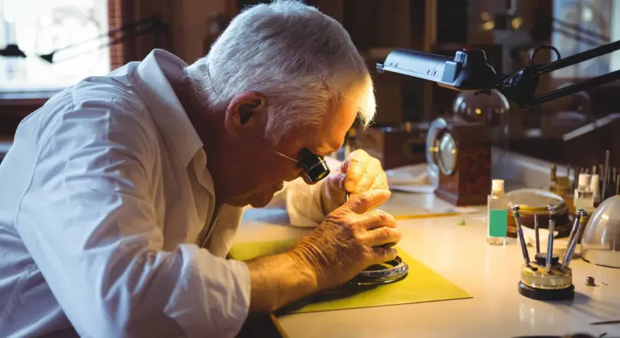 A watchmaker, wearing a loupe, meticulously works on a watch, demonstrating how to fix a watch with precision tools.