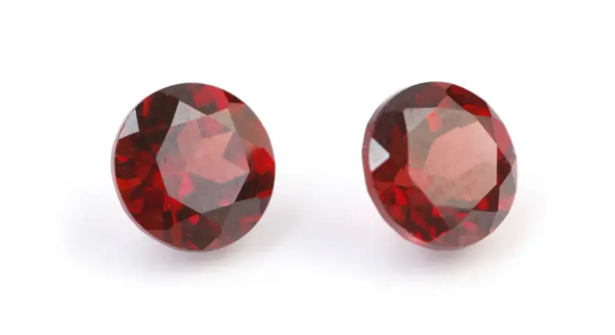 Two deep red, faceted gemstones, the traditional capricorn birthstone, are displayed on a white background.