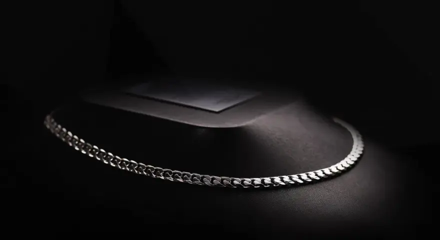 A sleek man platinum necklace rests on a dark, textured display.