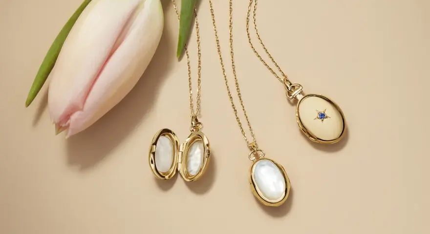 Gold lockets featuring mother of pearl, a lustrous material from shells, lie beside a delicate pink tulip.