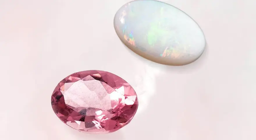 Two oval gemstones, a pink tourmaline and a white opal, are displayed. The opal's play-of-color makes it a perfect october 27 birthstone.