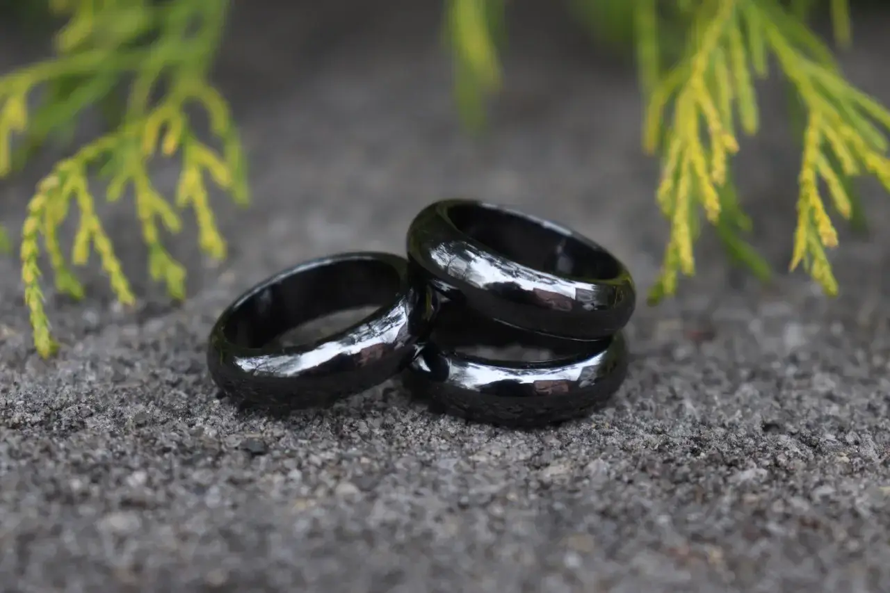 Three shiny hematite rings rest on a textured surface, with green foliage in the background. The hematite ring meaning is often associated with grounding and protection.