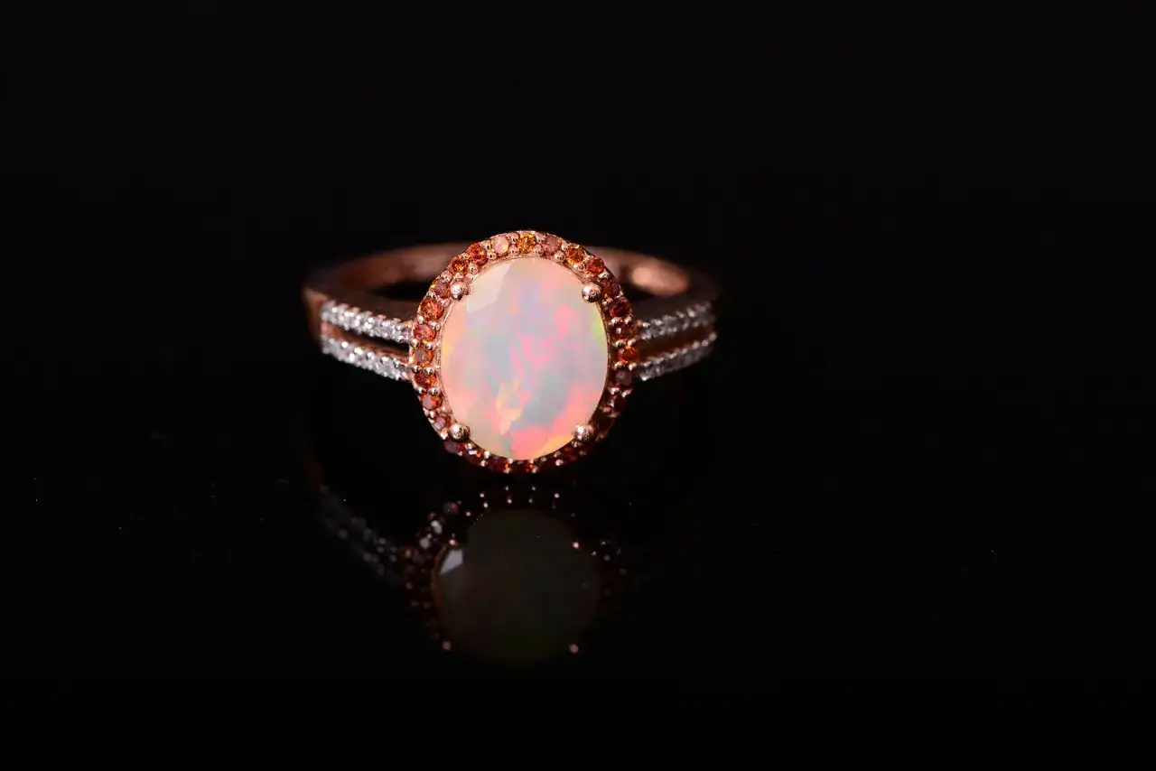 A rose gold ring with an opal center stone and a halo of smaller stones. This beautiful ring might explain why October has two birthstones: opal and tourmaline.