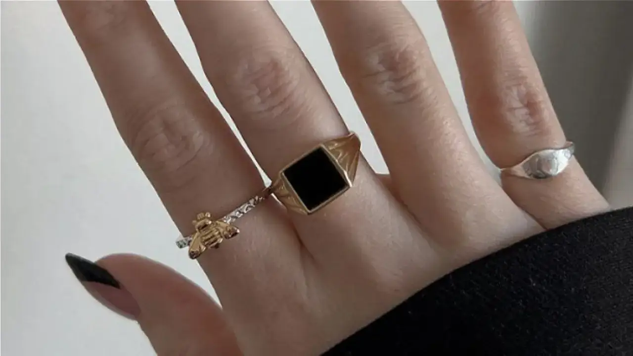 A hand adorned with rings, including a gold bee and a signet ring with a black stone. This look proves rose gold is far from out of style.