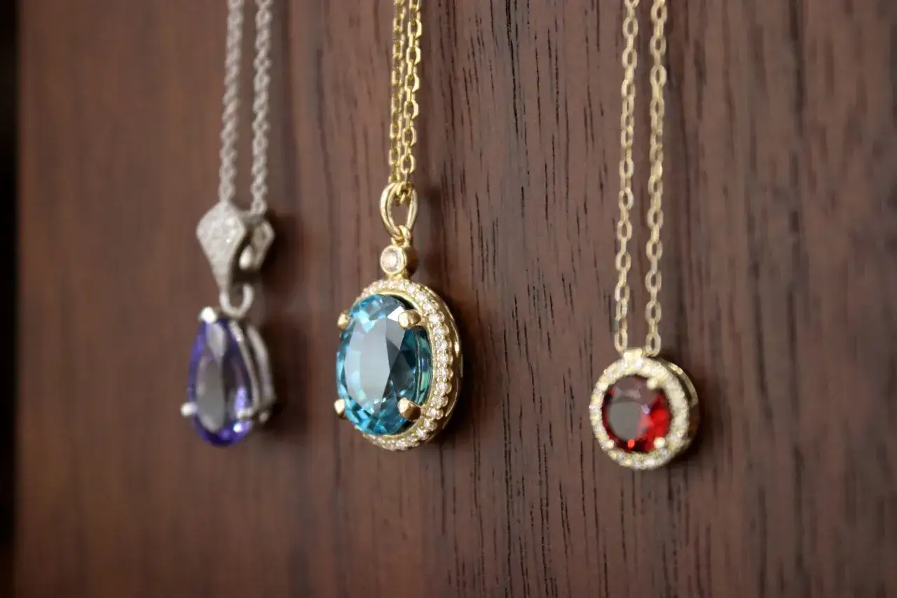 Three elegant pendants hang on chains. The leftmost features a pear-shaped purple stone, possibly a tanzanite, a popular capricorn birthstone.