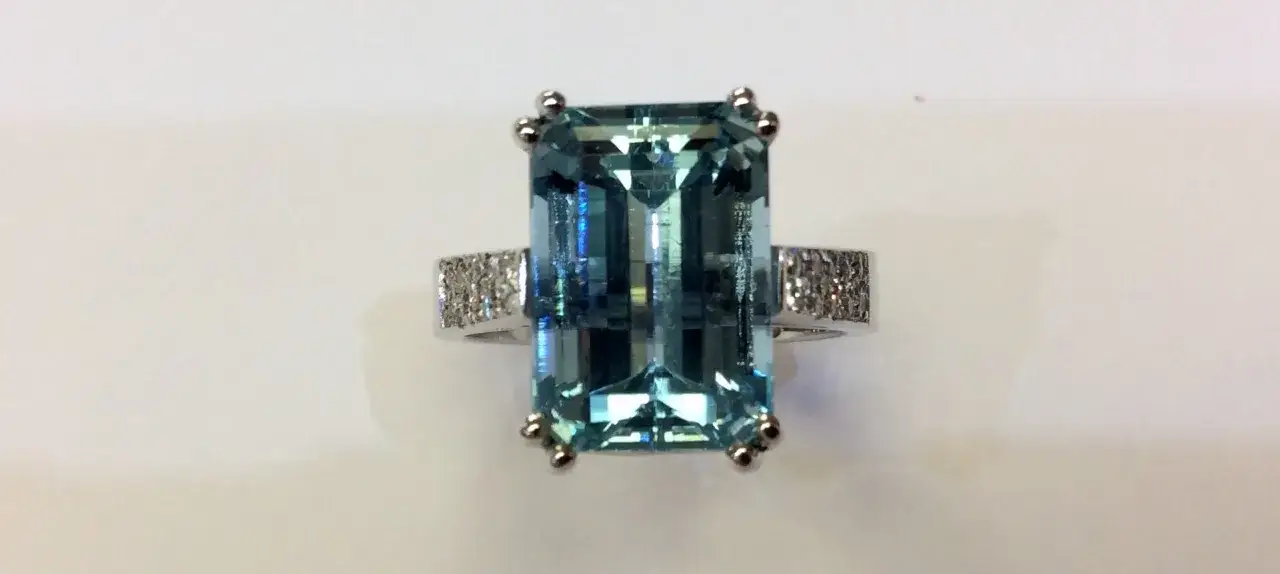 A stunning emerald-cut aquamarine ring, the march 6 birthstone, is set in white gold with diamond accents on the band.