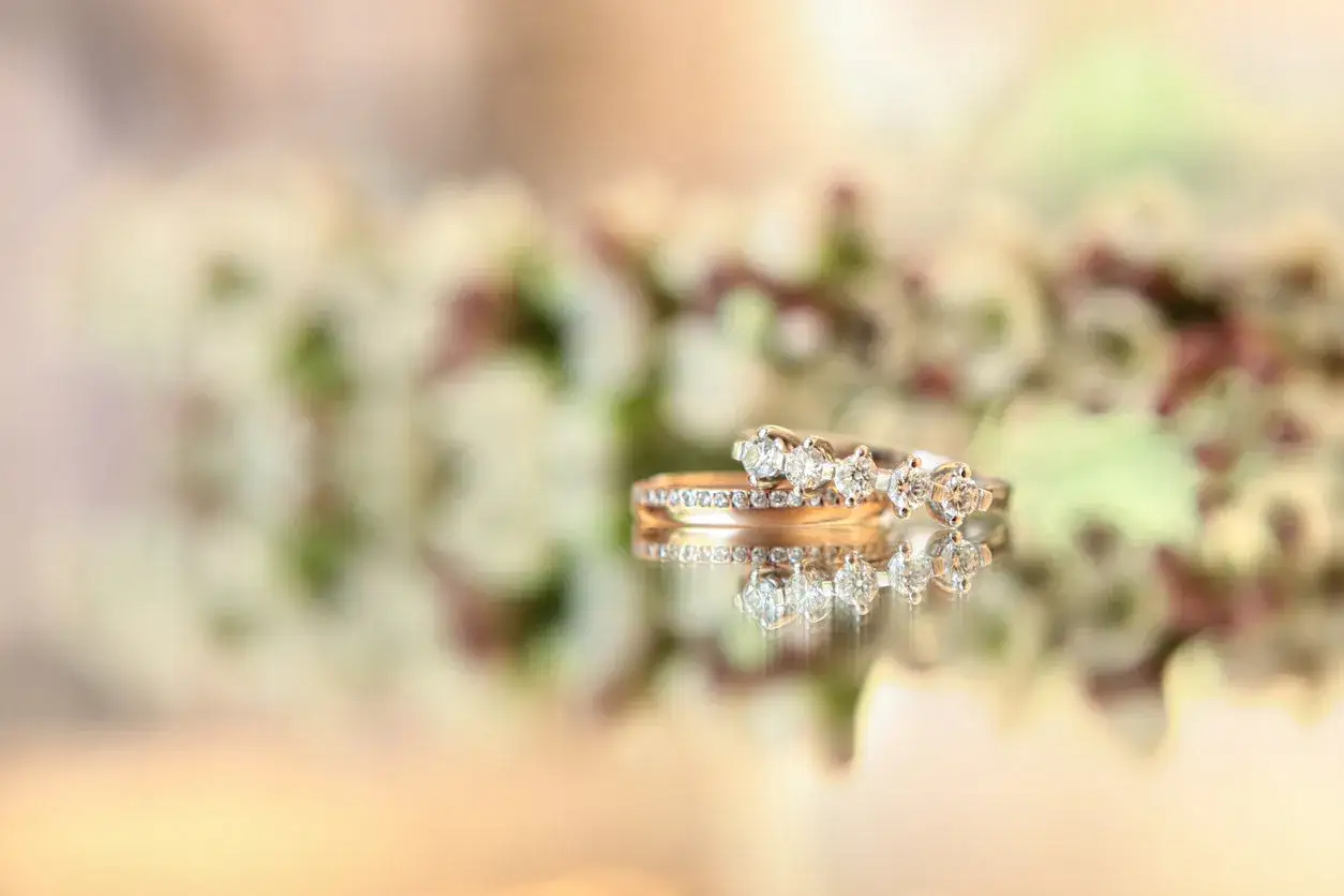 Two diamond rings, one a simple band and the other a trilogy, rest on a reflective surface, hinting at what is a promise ring.