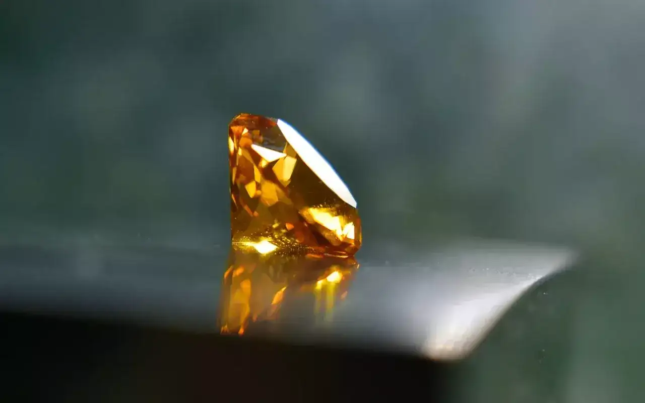 A faceted pukhraj stone, glowing with warm amber light, reflects on a polished surface.