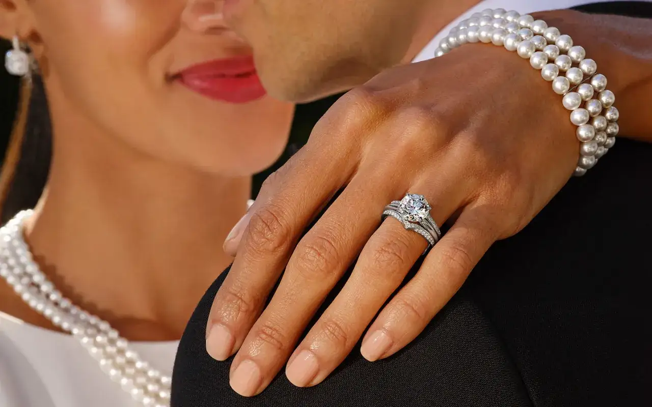 A hand adorned with a sparkling diamond ring and pearl bracelet, showcasing the beauty of lab grown vs natural diamond.