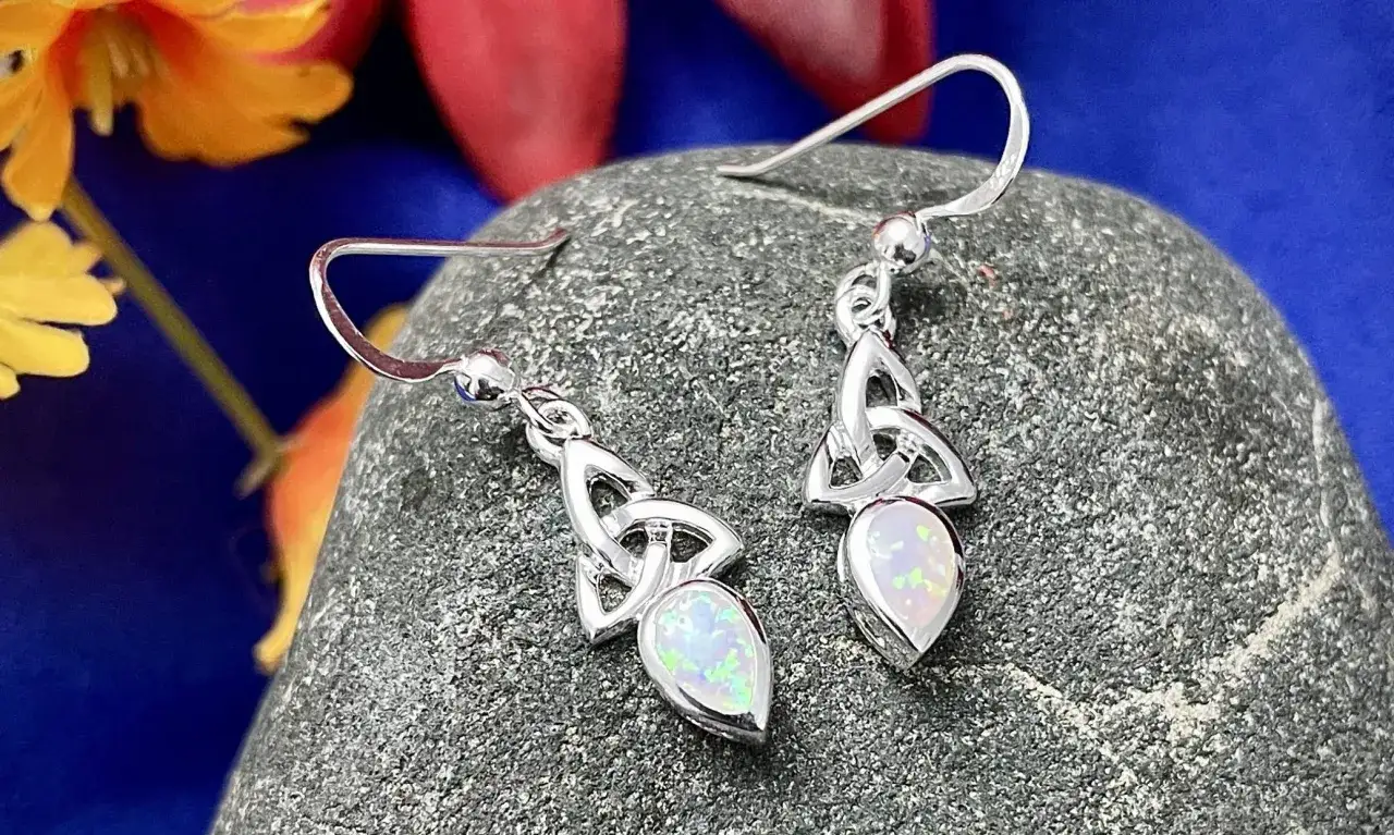 Silver earrings with Celtic knotwork and opals, reminiscent of Celtic birthstones, rest on a textured stone.