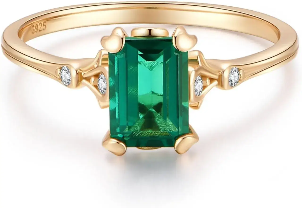 A stunning gold ring featuring an emerald, the may 13 birthstone, flanked by tiny diamonds.