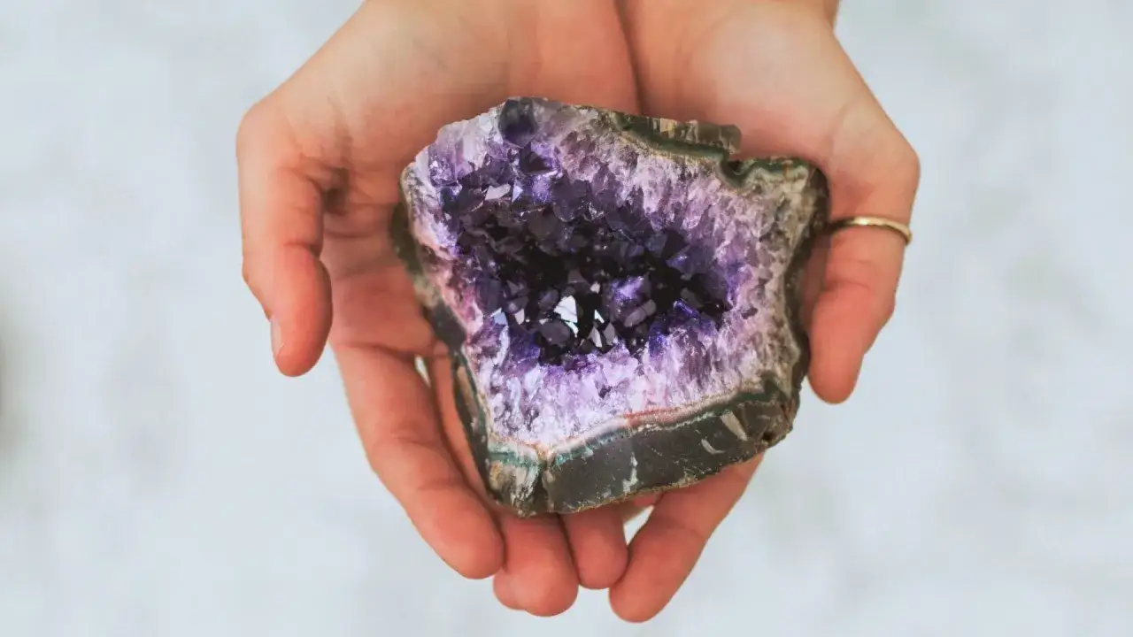 Hands cradle a geode, revealing a cavity lined with sparkling purple amethyst crystals. You can find amethyst in Brazil, Uruguay, and other locations worldwide.