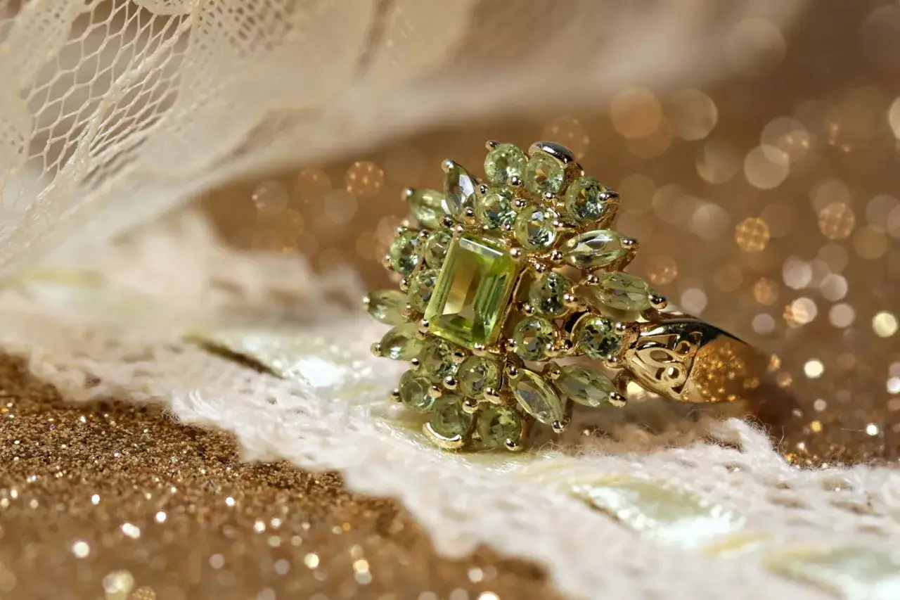 A dazzling ring featuring the august 3rd birthstone, peridot, surrounded by smaller gems on a bed of lace and glitter.