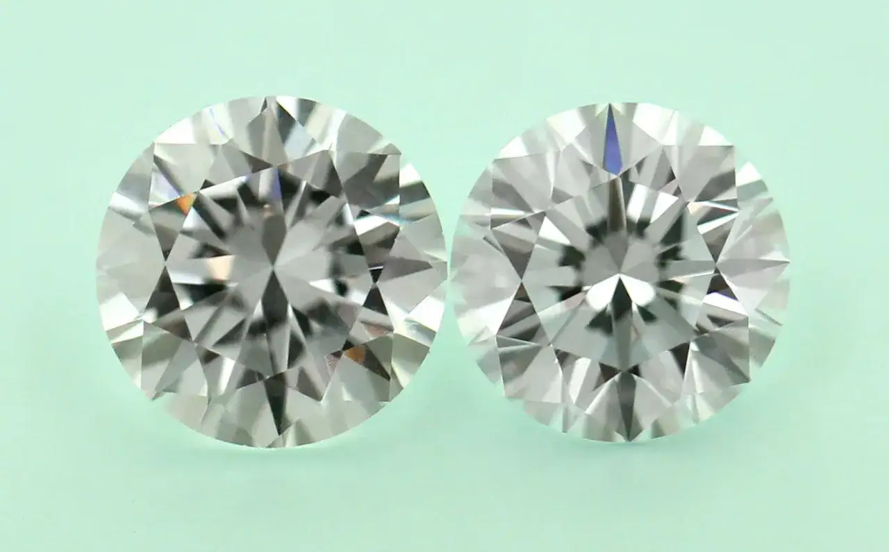 Two brilliant-cut simulated diamonds sparkle against a pale green background, showcasing their facets and fire.