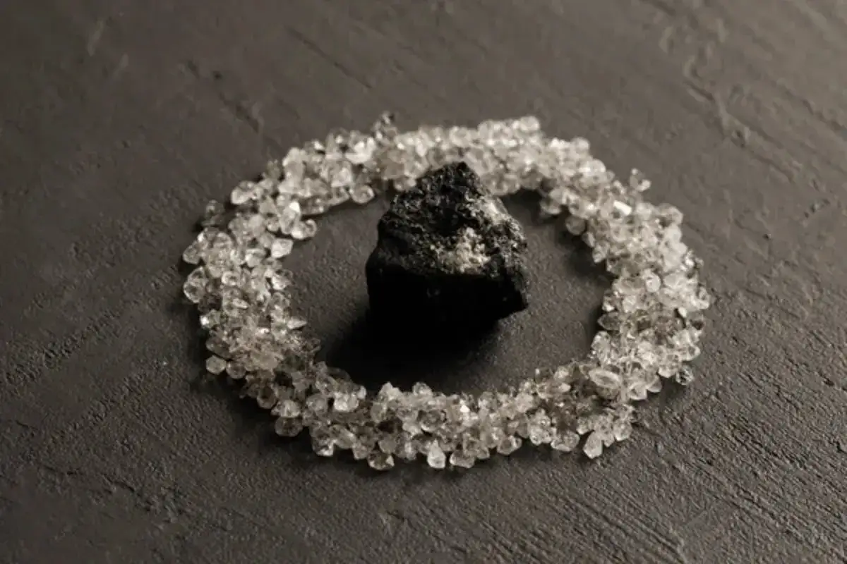 A rough black spinel sits at the center of a circle of small, clear crystals, hinting at the stone's protective black spinel meaning.