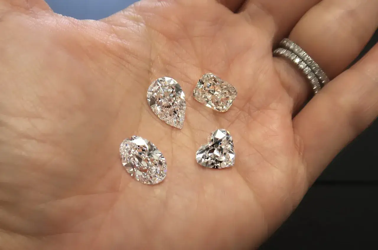 Four sparkling stones, each a unique cut, rest on a palm. One is heart-shaped, another a pear, and two are cushion-cut.