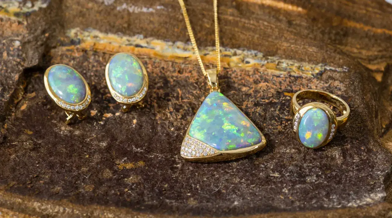 A set of gold jewelry featuring iridescent opal stones and diamonds. The collection includes oval earrings, a triangular pendant, and an oval ring.