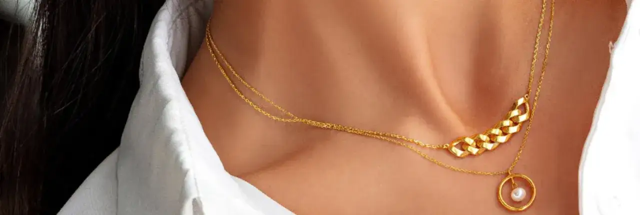 A guide choosing necklaces for necklines: layered gold chains with a pearl pendant complement a white shirt's collar.