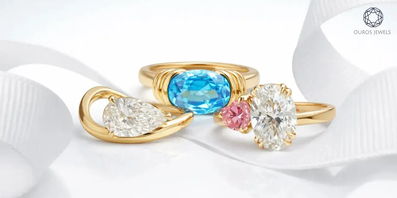 Three elegant gold rings showcase diverse styles of engagement rings: a pear-shaped diamond, a blue oval gem, and an oval diamond with a pink heart accent.