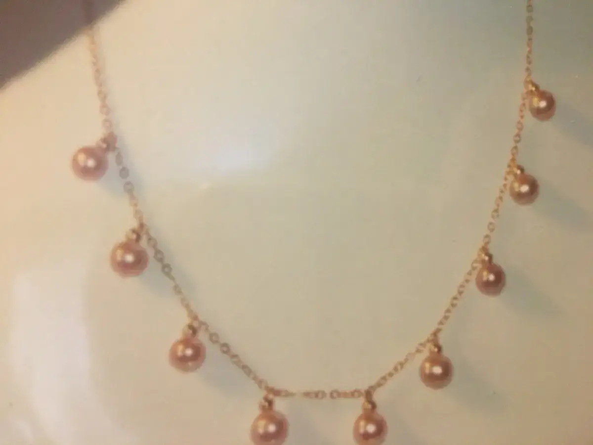 Delicate rose gold necklace with dangling pink pearls, symbolizing love and purity.
