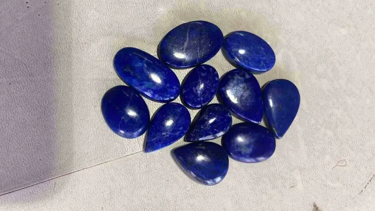 A collection of polished, deep blue Afghanistan gemstones, likely lapis lazuli, arranged on a textured surface.