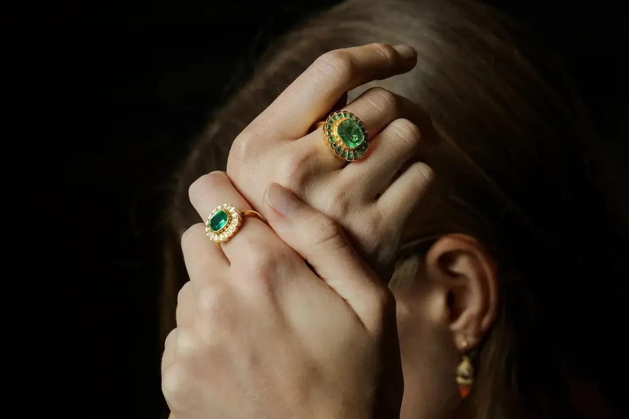 Hands adorned with gold rings featuring vibrant emeralds, symbolizing love, rebirth, and prosperity.