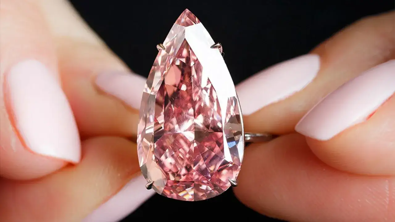 A pear-shaped pink diamond, possibly the most expensive gemstone, held between manicured fingers.